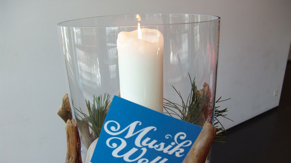 Weisse Kerze in einem Glas als Adventschmuck. Im Vordergrund das Logo von SRF Musikwelle.