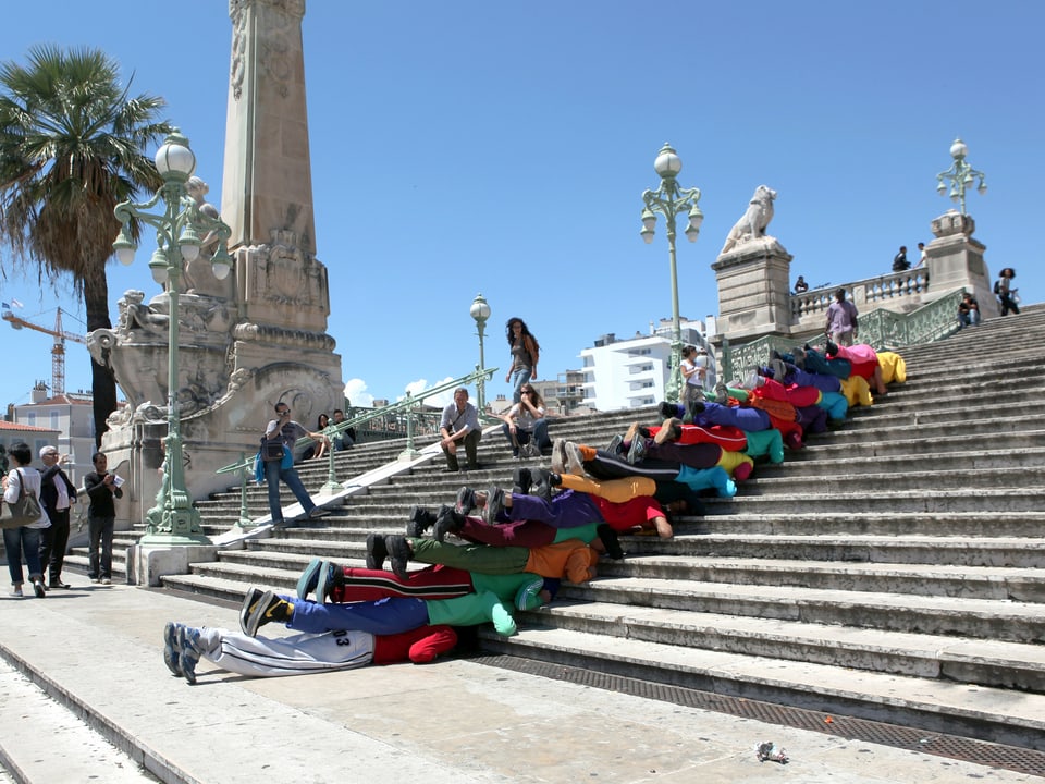 Menschen liegen aufeinander auf einer Treppe.
