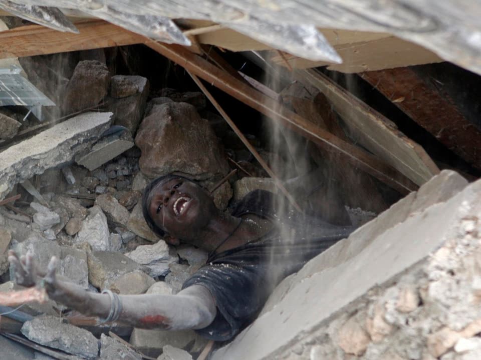 Ein Überlebender unter Trümmern streckt seine Hand aus.