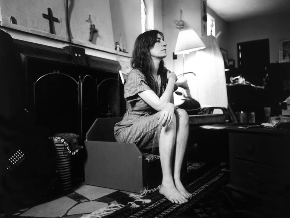 Patti Smith sitzt in jungen Jahren auf einem kleinen Hocker und schaut aus dem rechten Bildrand.