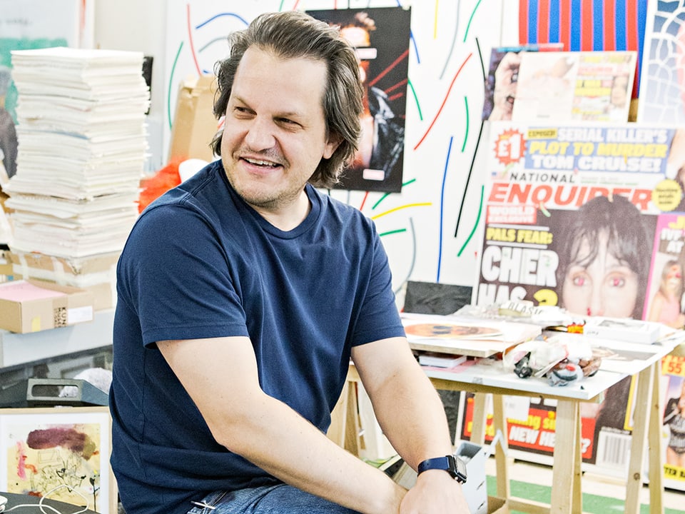 Der Künstler Beni Bischof, sitzend in seinen Atelier, lachend zur Seite schauend.
