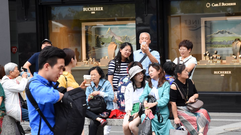 Eine Gruppe asiatischer Touristen sitzt vor den Schaufenstern eines Uhrengeschäfts