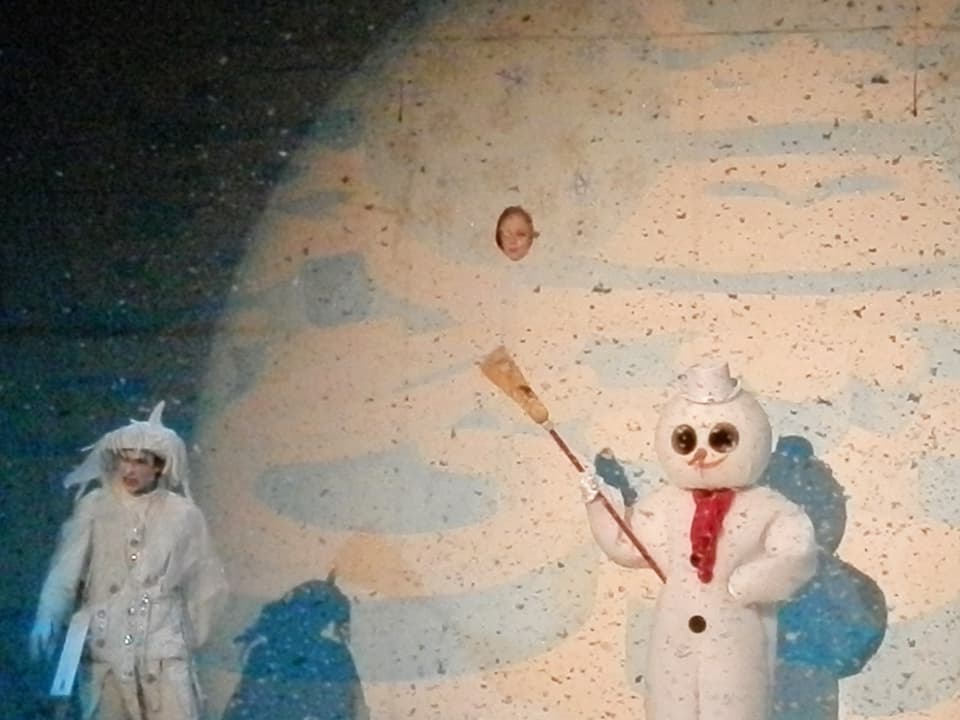 Die weisse Figur des Winters und ein Schneemann, aus einem Gucklock schaut ein Kind.