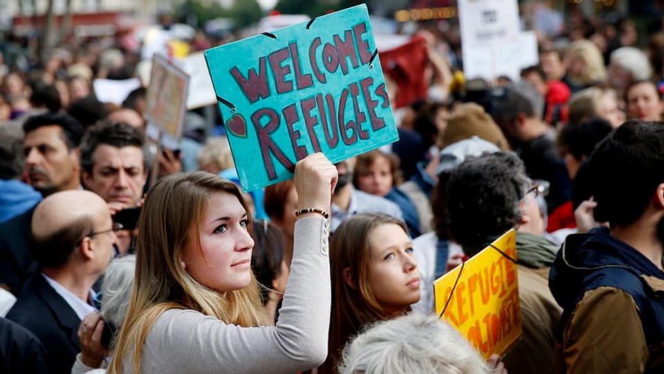 Frau mit Plakat in Menschenmenge: Welcome Refugees