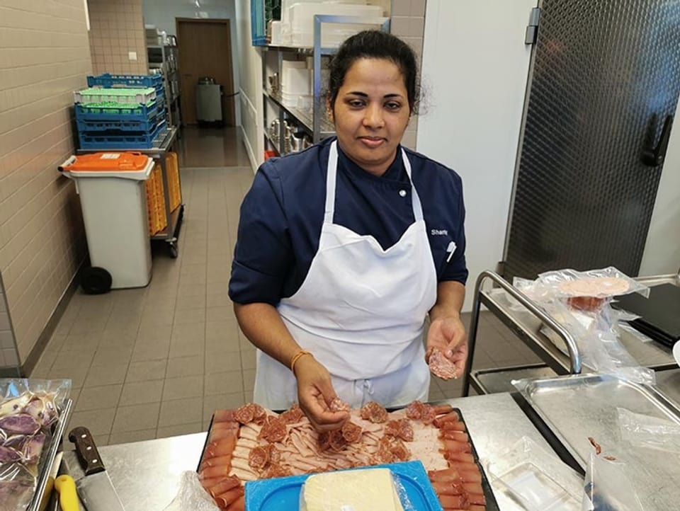 Küchenmitarbeiterin bereitet eine Fleischplatte vor.