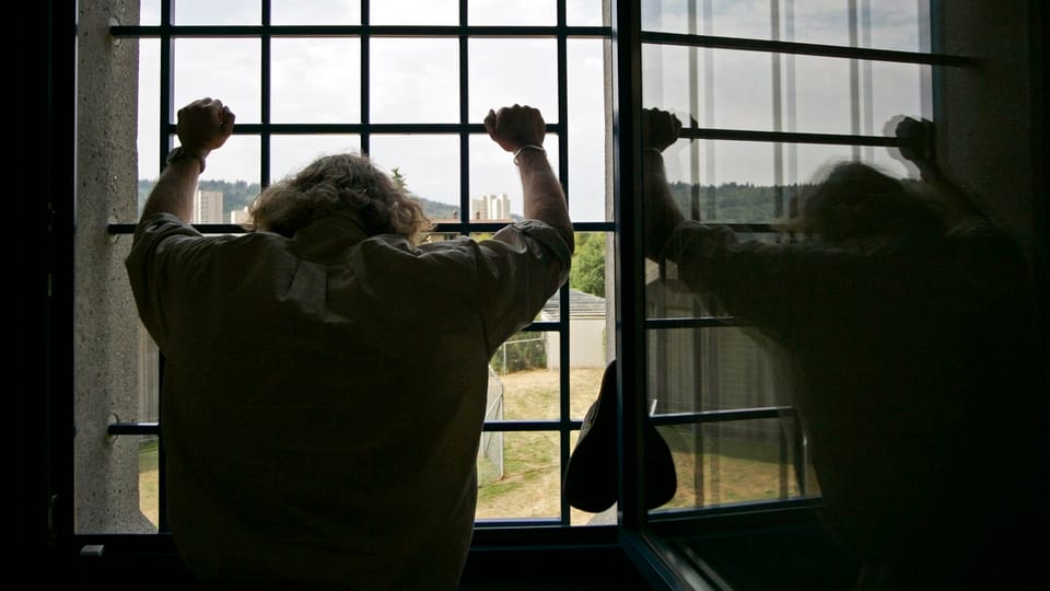 Rückenansicht eines Häftlings, der an einem vergitterten Fenster steht.
