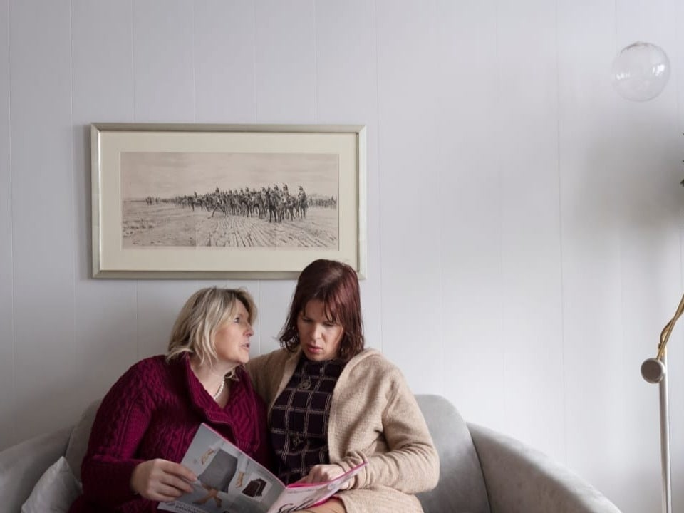 zwei Frauen sitzen auf dem Sofa und schauen sich Fotobücher an