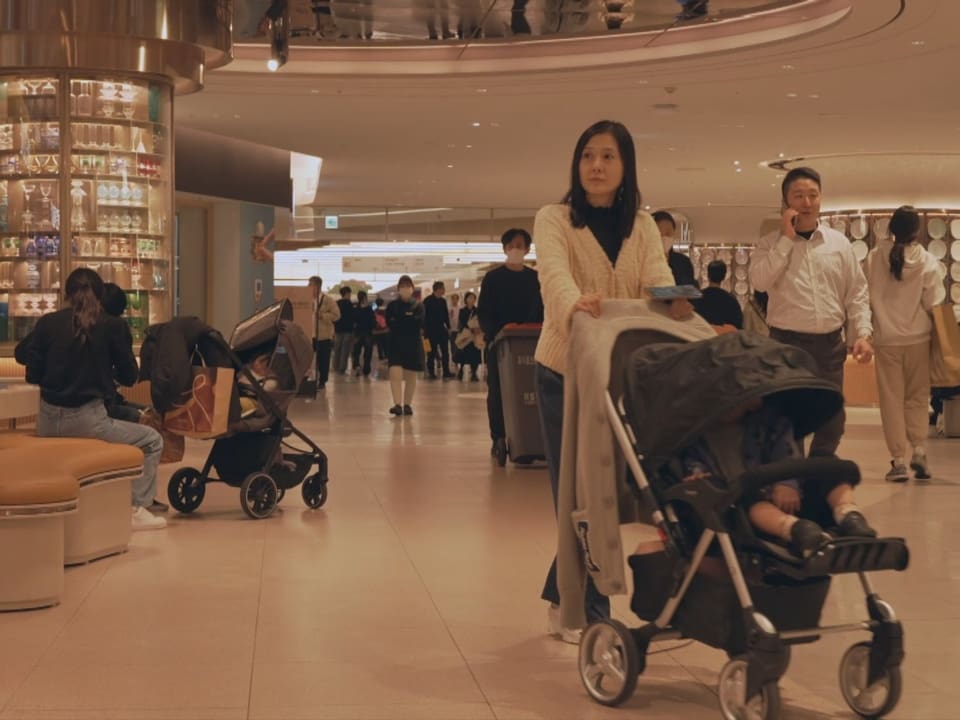 Menschen in einer belebten Einkaufszentrum-Passage mit Kinderwagen.