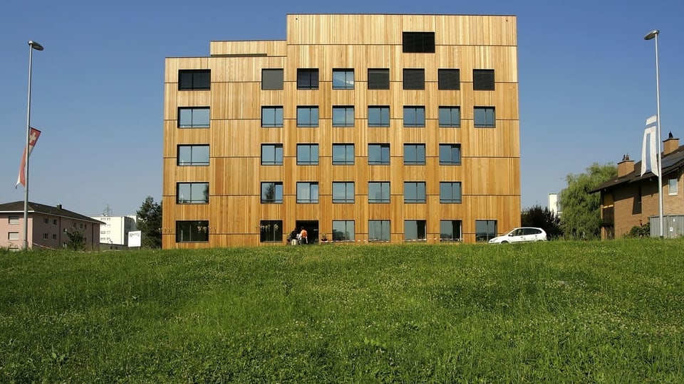 Ein grosses Mehrfamilienhaus, komplett aus Holz gebaut. Davor eine grüne Wiese.