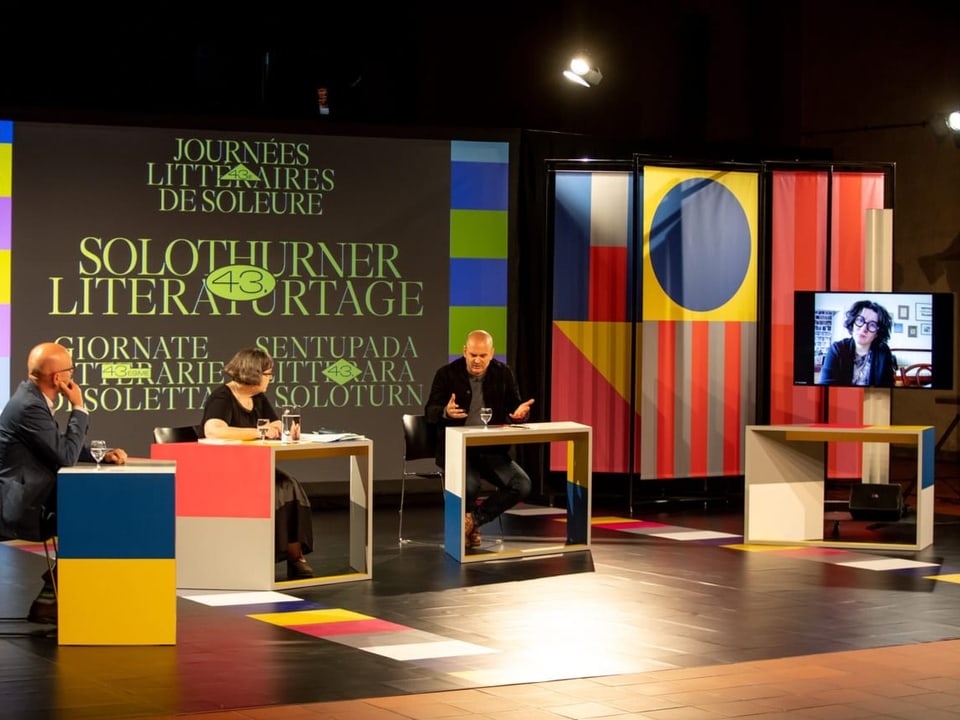 Der Autor Jonas Lüscher sitzt auf einer Bühne mit anderen Gesprächspartnern.