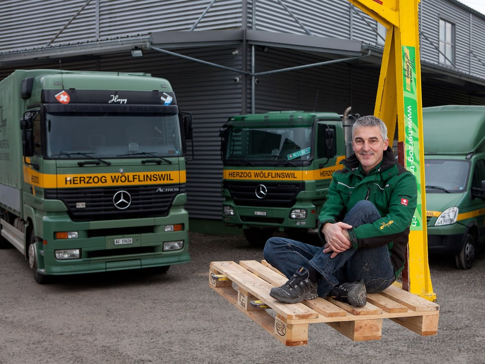 Adrian Herzog posiert vor drei Lastwagen seines Unternehmens.