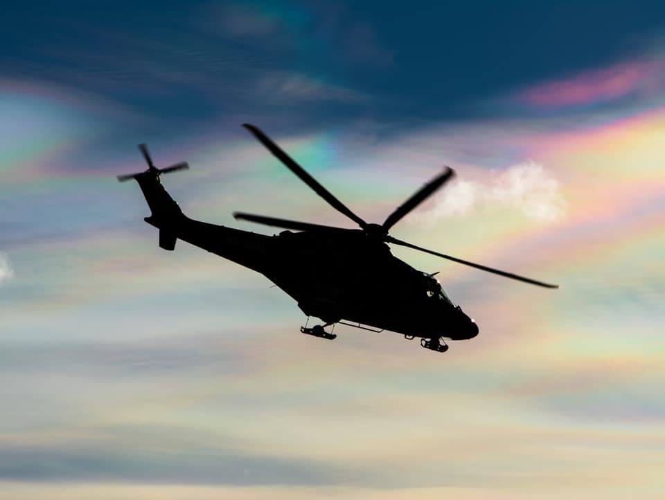 Farbige Wolken im Hintergrund, im Vordergrund ein schwarzer Helikopter.