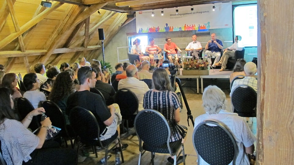 Publikum im Dachstock einer Scheune, dahinter Podium mit Schülern und Experten.