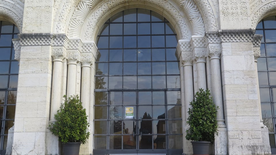 Der Eingang der Kirche mit Bögen aus weissem Stein, darin ein halbrundes Fenster, das vergittert ist.
