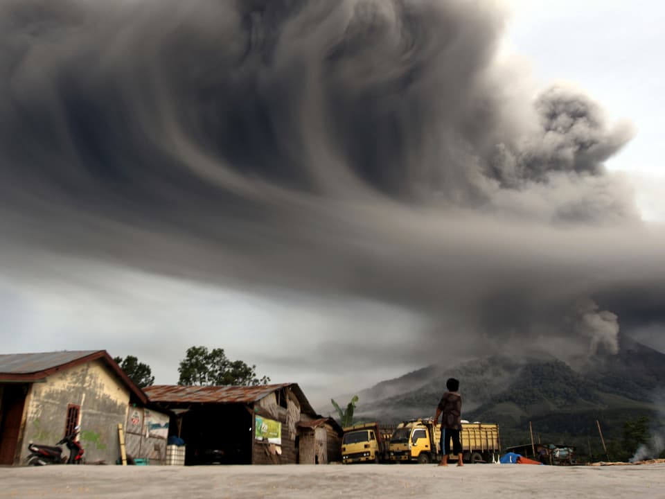 Ein Junge steht auf einem Platz in einem Dorf nahe des Vulkans. Eine gewaltige Aschewolke schiebt sich über das Dorf. (reuters)