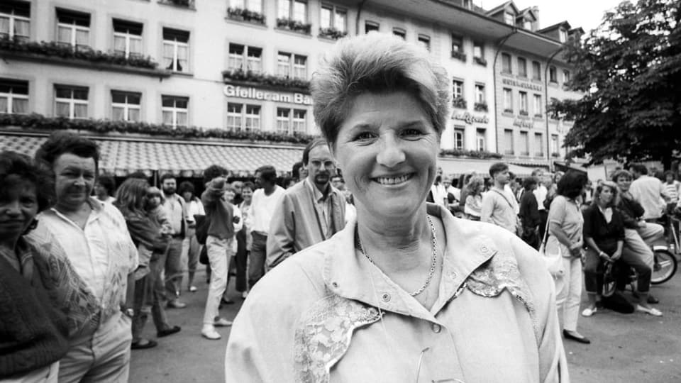 Schwarzweissbild: Lächelnde Frau mit kurzen Haaren auf einem Platz mit vielen Leuten.