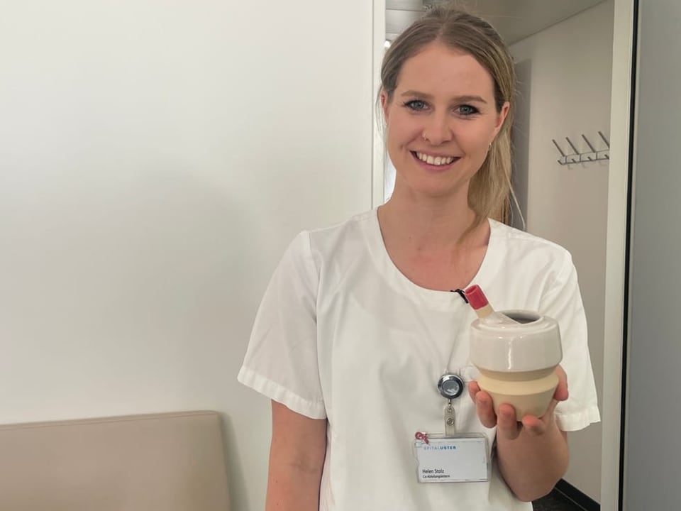 Lächelnde Krankenschwester mit Namensschild hält medizinisches Gerät.