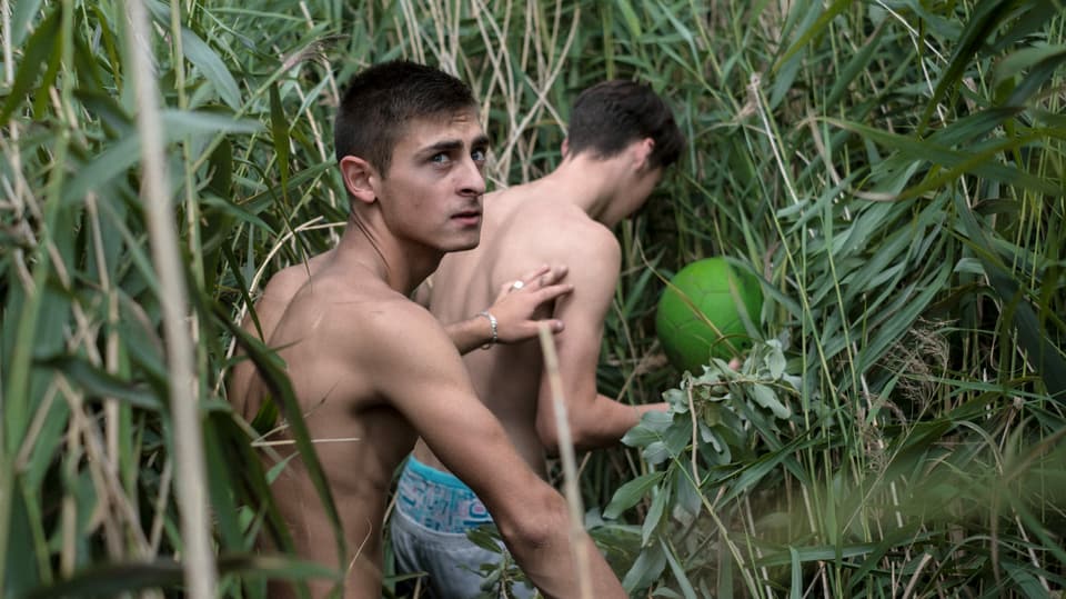 Zwei junge Männer schlagen sich mit einem Ball durchs hohe Grass. 