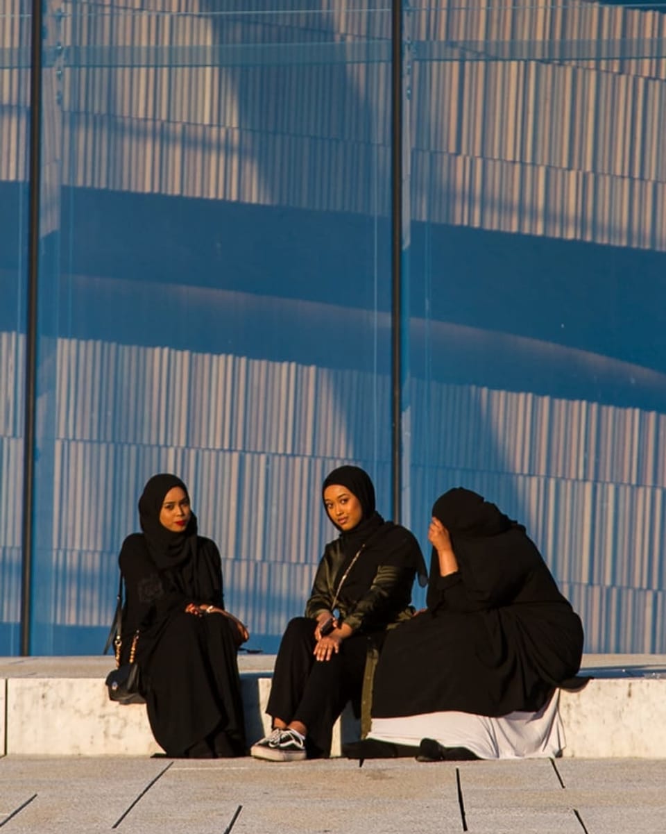 Drei Frauen mit Kopftücher sitzen auf einer Bank vor einem Haus.