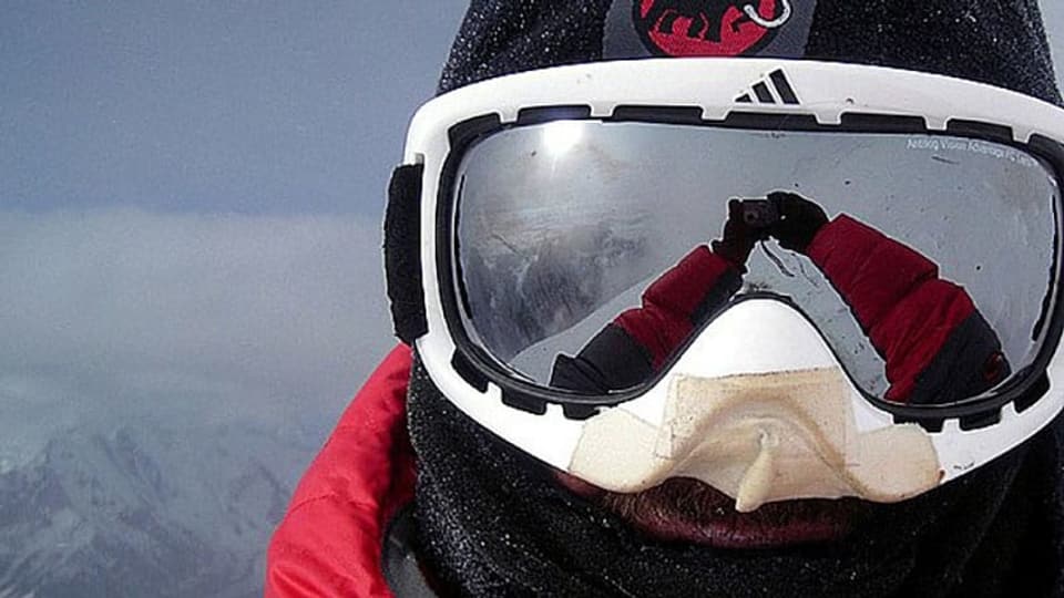 Ein Selfie mit einer Skibrille. Im Visier spiegelt sich die umliegende Bergwelt und die Sonne.