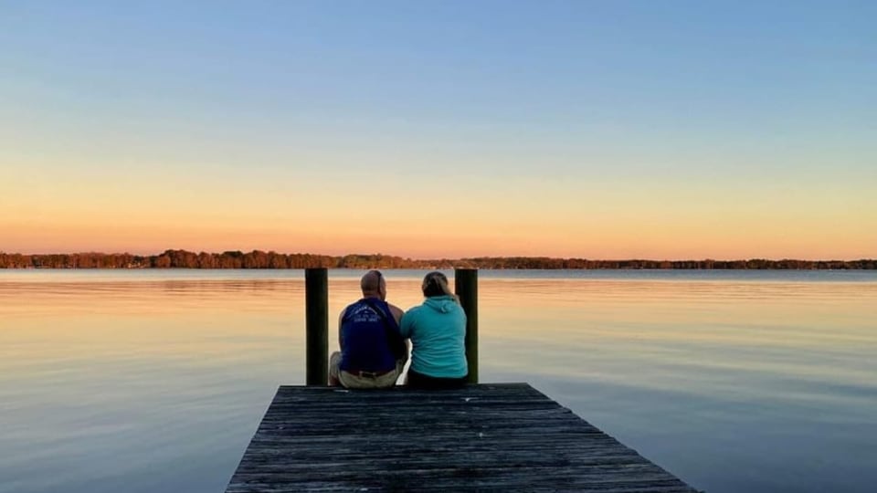Marina Marrer und Mike Hostettler sitzen beim Sonnenuntergang auf einem Holzsteg.