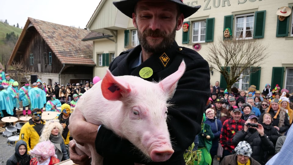 Ein Mann mit einem Schwein auf den Armen.