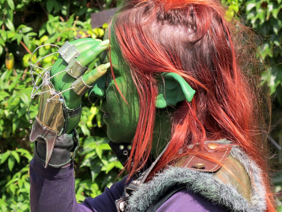 Frau, grün geschmickt, streicht sich mit geschmückter hand durch ihr rotes Haar