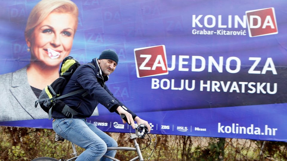 Mann fährt auf Velo vor Wahlplakat der Herausfordererin Kolinda Grabar Kitarovic vorbei.