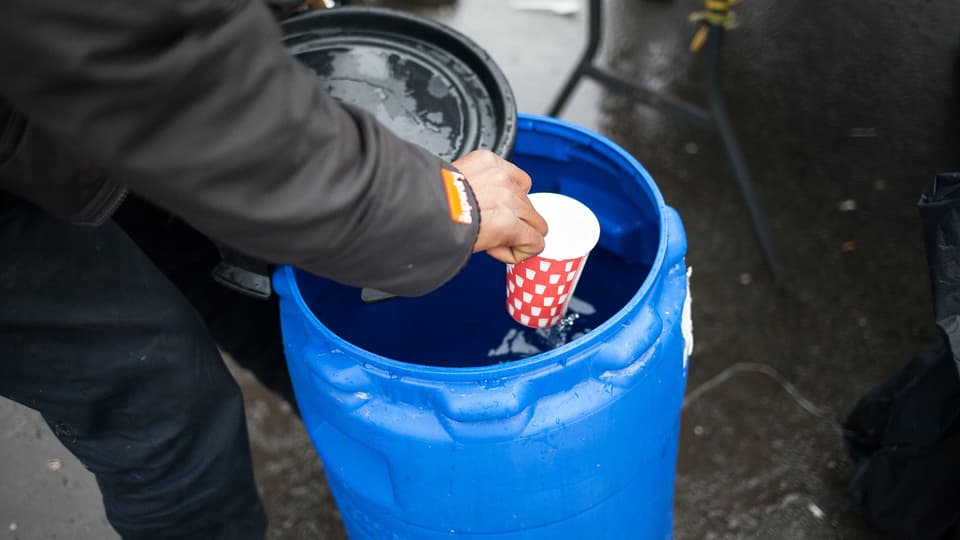 Eine Hand schöpft Wasser mit einem Becher aus einem blauen Kanister.