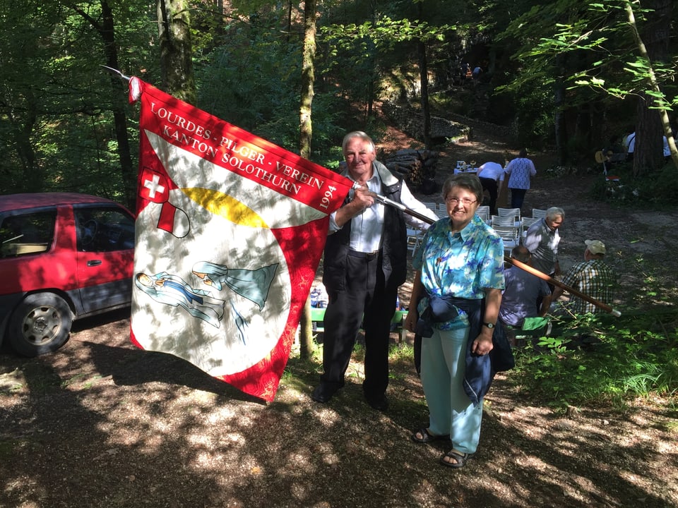 Frau und Mann mit einer Vereinsfahne stehen im Wald
