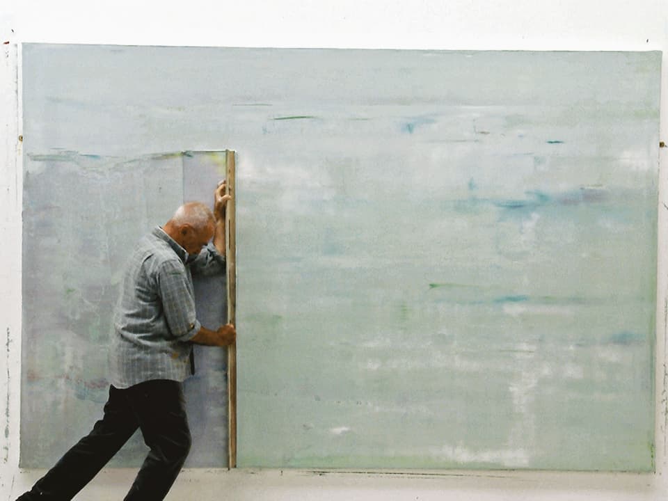 Richter schabt mit einem Brett die Farbe von einem grosse, abstrakten Gemälde.