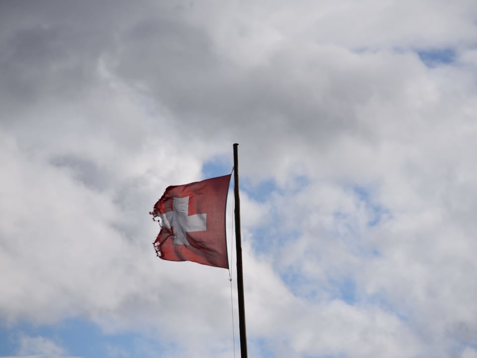 Eine beschädigte Schweizer Flagge vor dem bewölkten Himmel in Langnau im Emmental.
