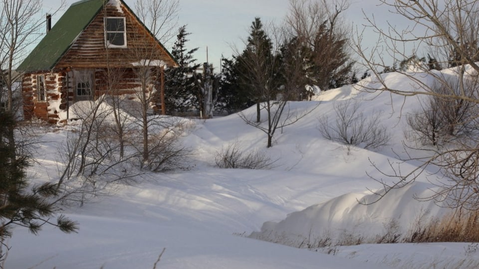 Eine verschneite Landschaft mit einem Haus hinten links.