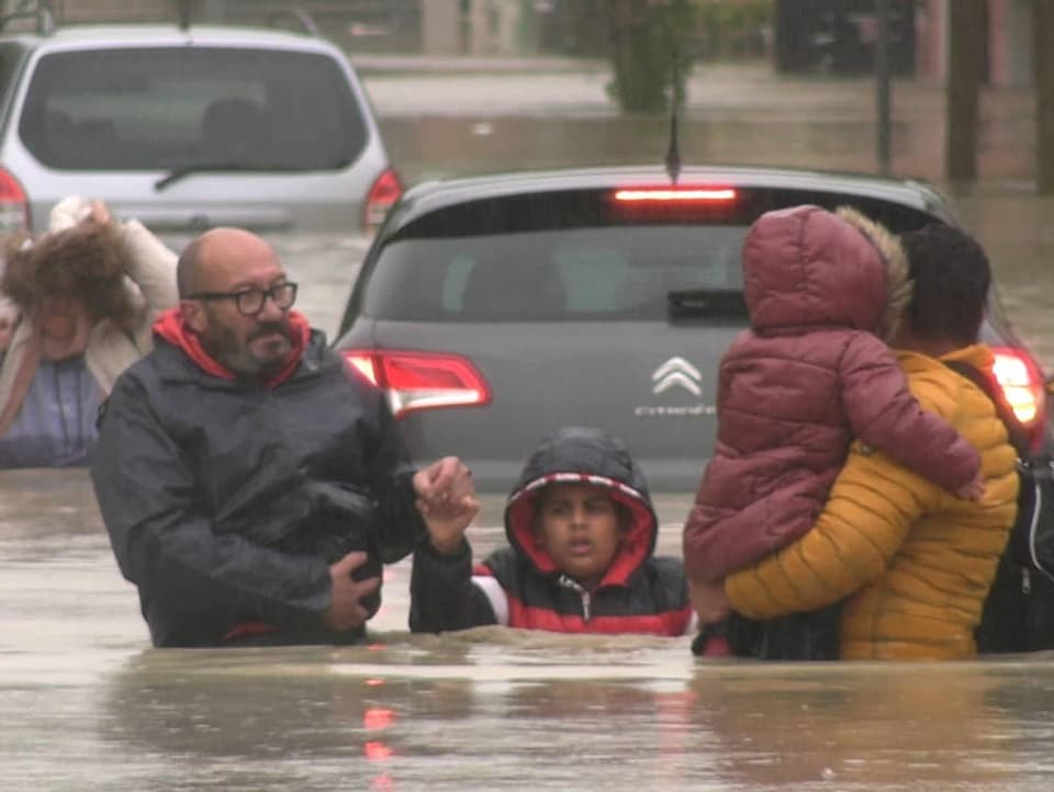 Familien mit Kindern watet durch überflutete Strasse.