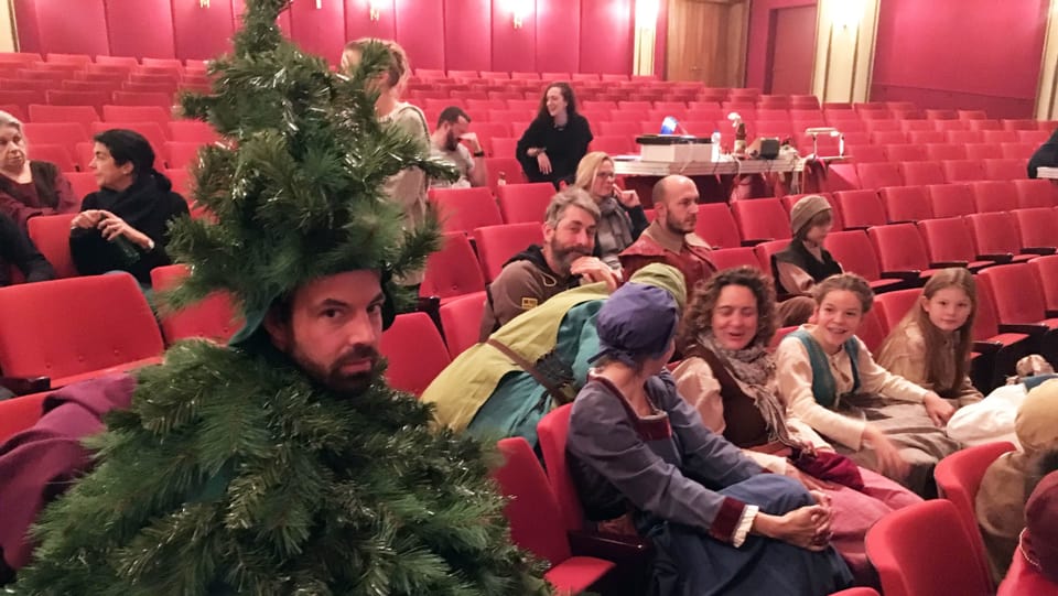 Ein als Tannenbaum verkleideter Mann sitzt im Zuschauerraum eines Theaters.