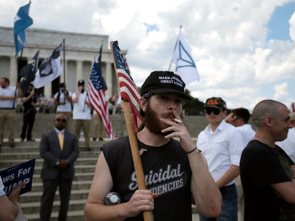 Ein junger Mann hält die amerikanische Flagge hoch, raucht eine Zigarette.