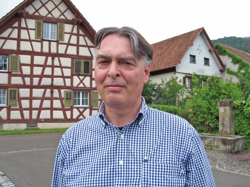 Jürg Biedermann vor beinem Fachwerkhaus und einem Dorfbrunnen.