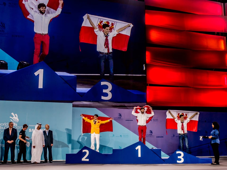 Drei Junge Männer stehen auf dem Siegerpodest. Zuoberst ein Schweizer mit Fahne. 