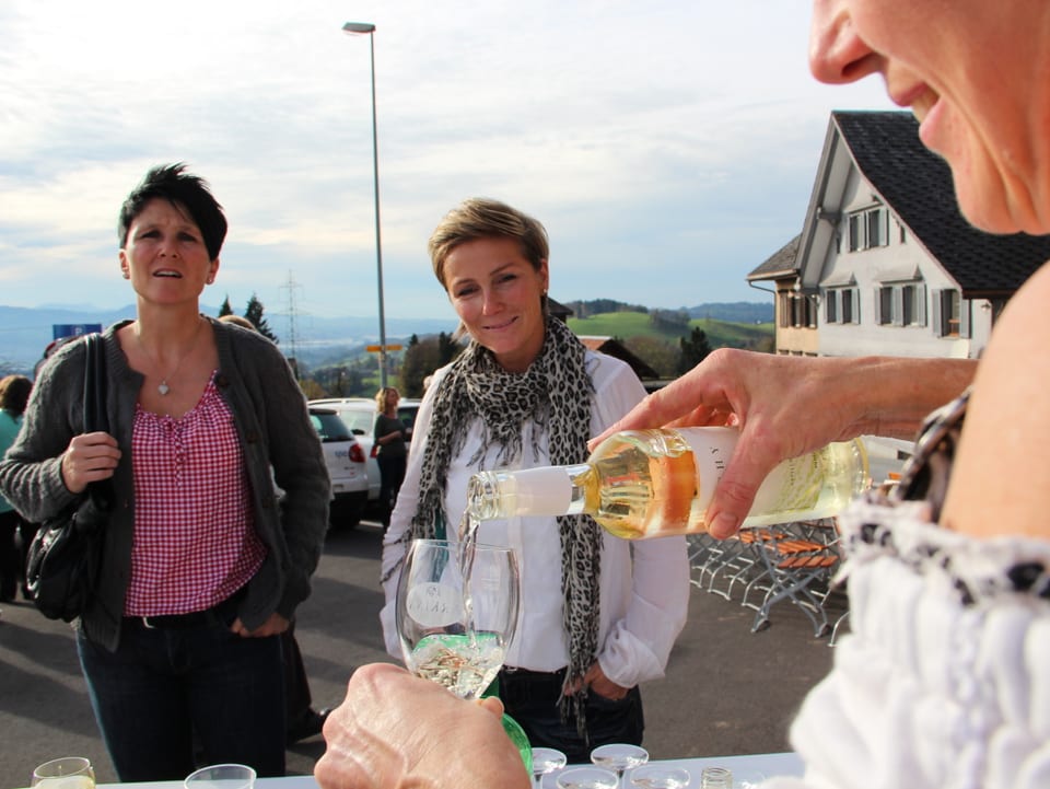 Eine Rüeterswilerin schenkt zwei weiteren Dorfbewohnerinnen ein Glas Wein ein.