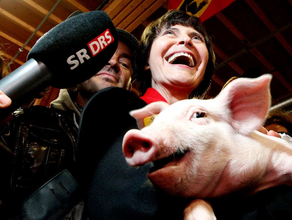 Calmy-Rey hält ein Schweinchen im Arm und lacht.