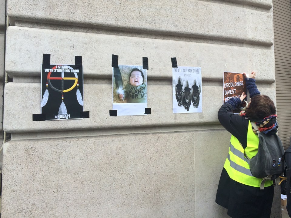 Einme Frau hängt mit Klebeband A4-Format-Proteste an die Wand.