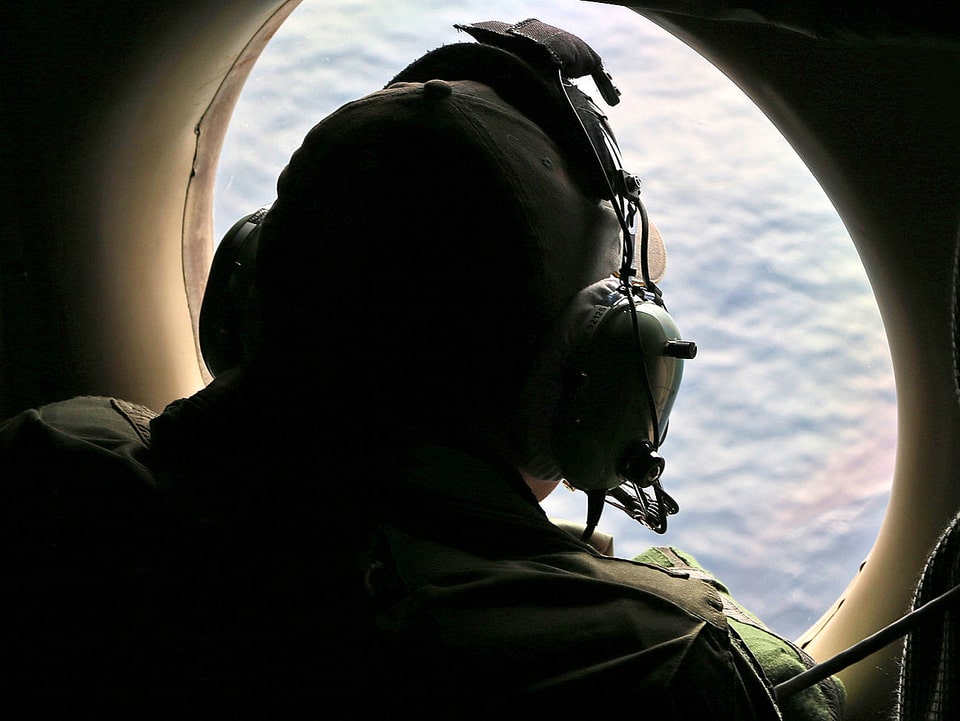 Suchexperte in einem Flugzeug. Er schaut auf das offene Meer hinunter.