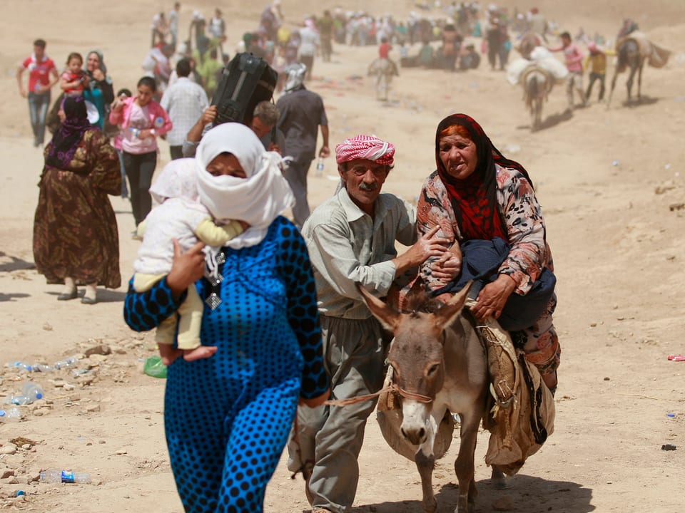 Flüchtlinge laufen durch wüstenartiges Gelände, teilweise auf Eseln.
