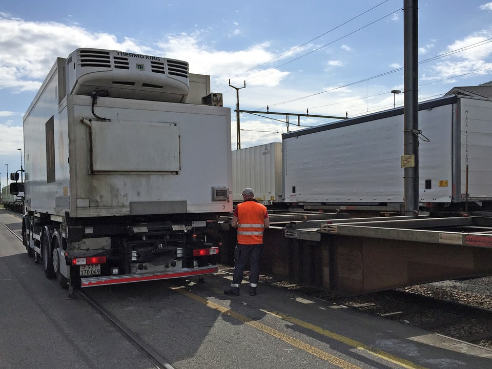 Lastwagen mit Kühlcontainer neben leerem Eisenbahnwagen