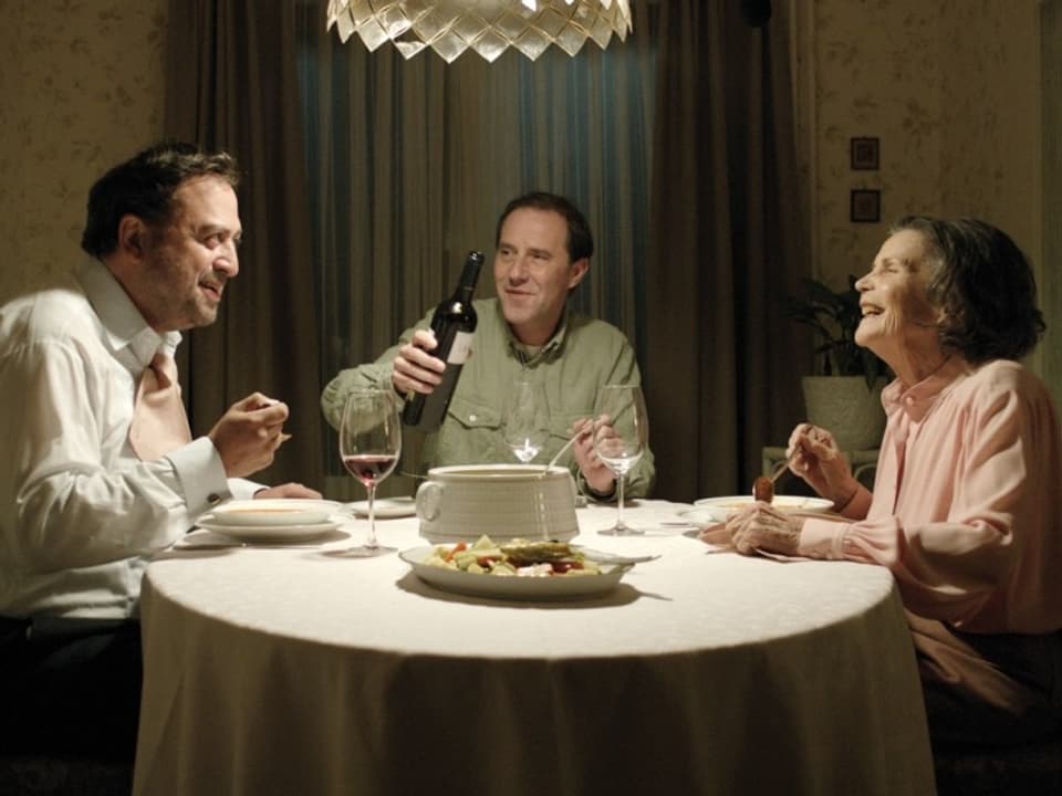 Ältere Frau mit zwei Männern am Tisch.