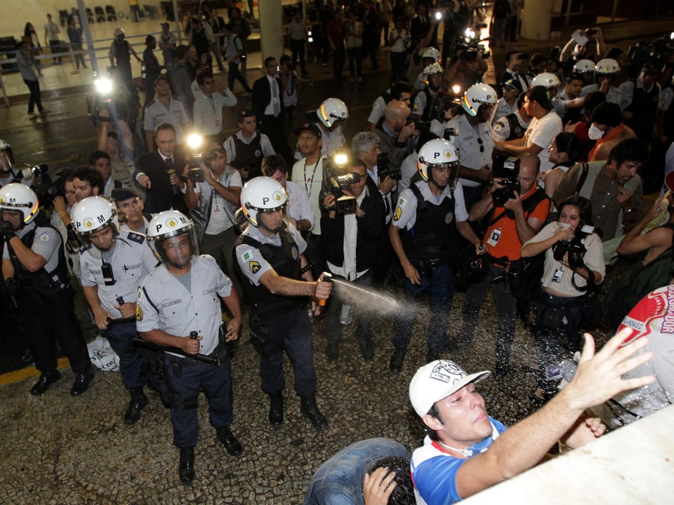 Polizisten und Demonstranten Auge in Auge, ein Polizist sprüht Pfefferspray in Richtung Protestierende.