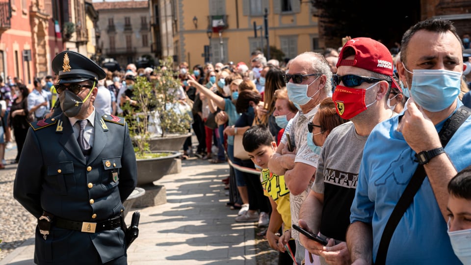 Menschenauflauf, viele tragen eine Gesichtsmaske, darunter auch ein Polizist.