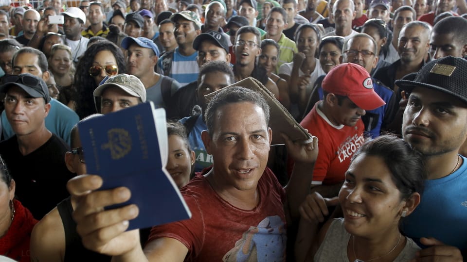 Eine risige Menschenmenge, vorne ein Mann, der einen kubanischen Pass hochhält.