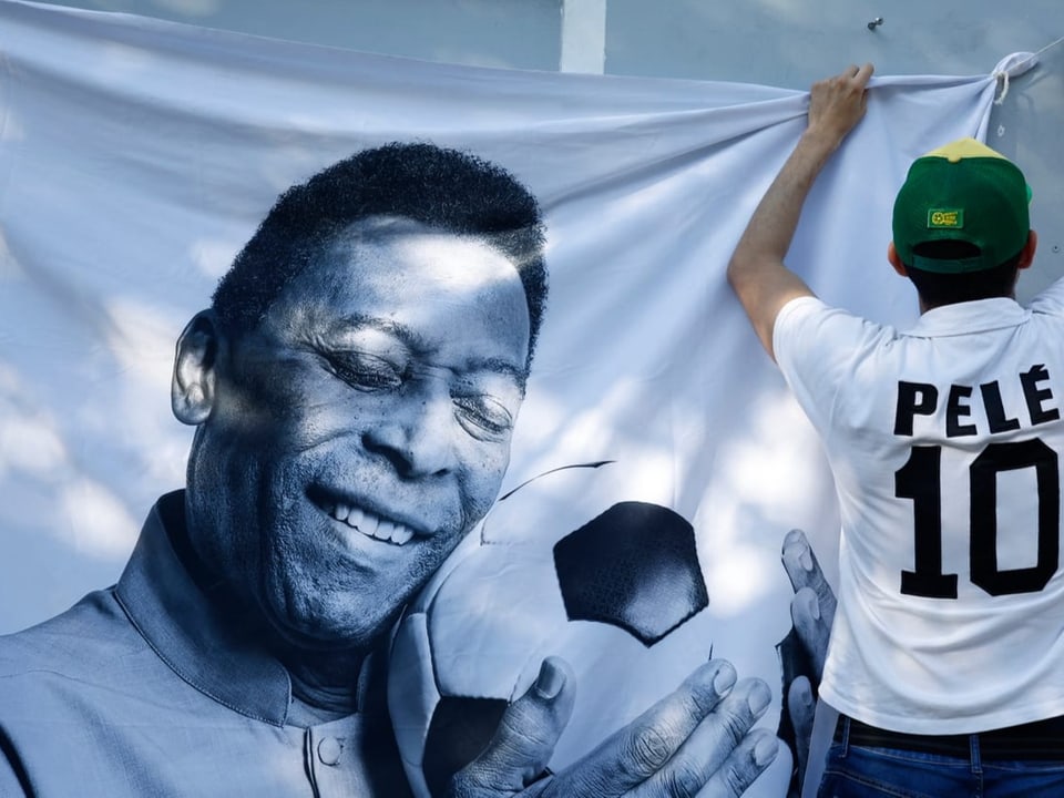 Ein Fan hängt ein Plakat mit Pelés Gesicht auf.