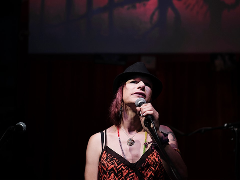 Eine Frau mit Hut steht auf der Bühne und singt ins Mikrofon.